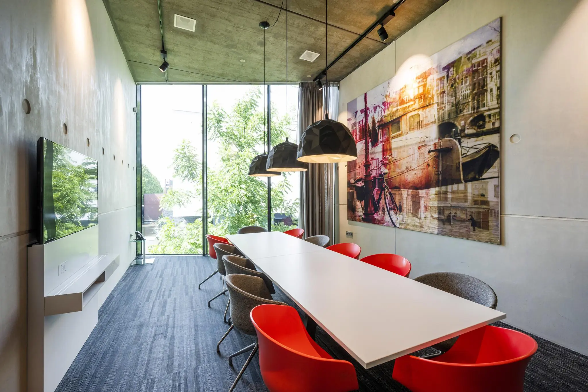 Moderne vergaderruimte aan de Fred. Roeskestraat met lange tafel, kleurrijke stoelen, grote ramen en een wanddecoratie met Amsterdams straatbeeld.
